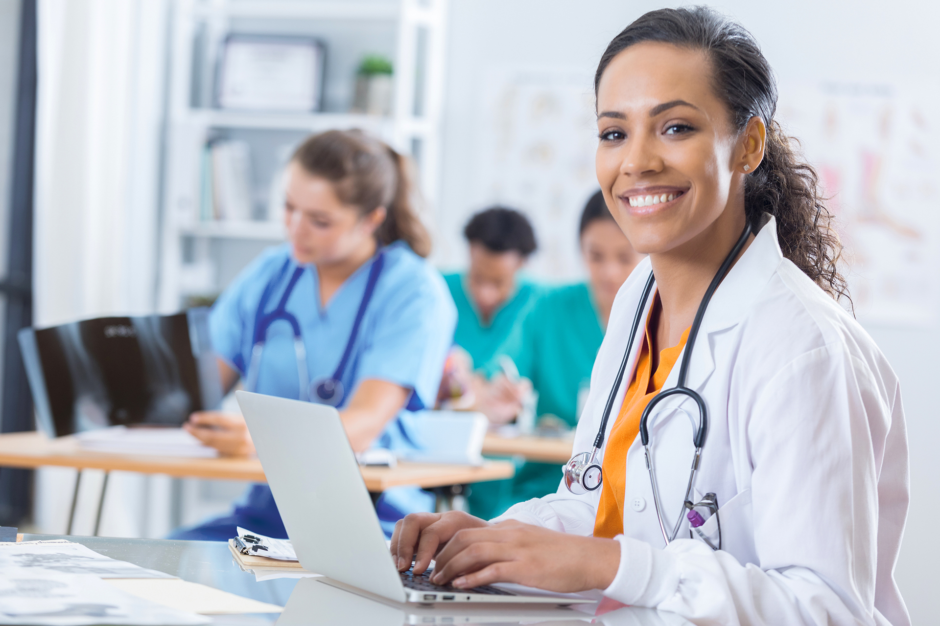 Beautiful African American female medical intern uses a laptop during class. She is smiling at the camera.